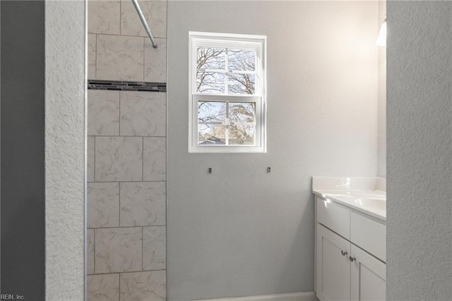 full bath with a textured wall, vanity, and a tile shower