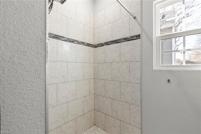 bathroom featuring tiled shower and a textured wall