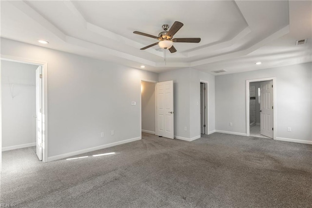 unfurnished bedroom with a tray ceiling, carpet flooring, baseboards, and visible vents