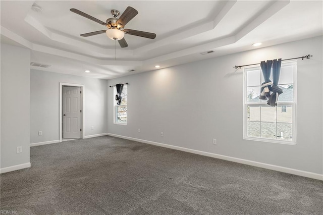 unfurnished room featuring a tray ceiling, baseboards, visible vents, and dark colored carpet