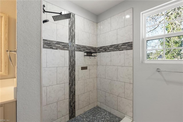 bathroom with a textured wall, vanity, and a tile shower