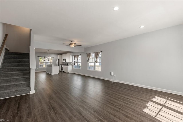 unfurnished living room featuring stairs, dark wood-type flooring, baseboards, and a wealth of natural light