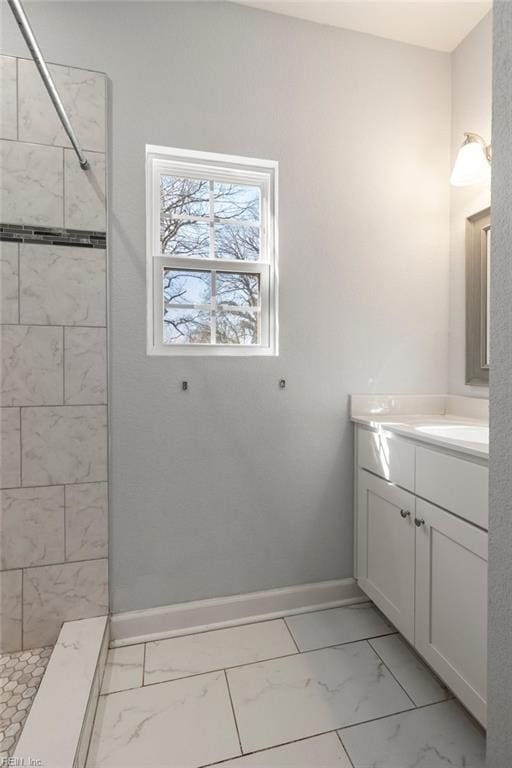 full bath featuring a tile shower, marble finish floor, vanity, and baseboards