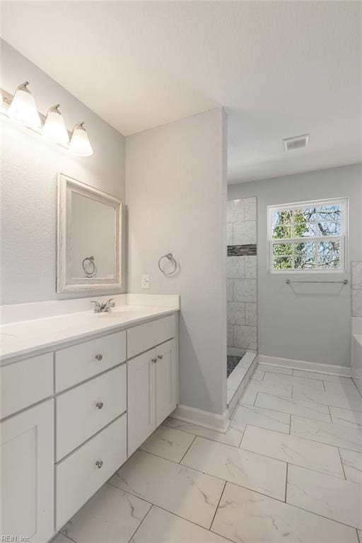 bathroom with baseboards, tiled shower, double vanity, a sink, and marble finish floor