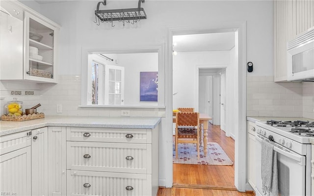 kitchen with white appliances, light wood finished floors, white cabinets, glass insert cabinets, and backsplash