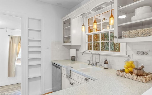 kitchen with a sink, stainless steel dishwasher, backsplash, light countertops, and glass insert cabinets