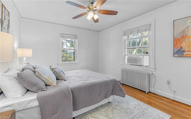 bedroom with radiator, ceiling fan, baseboards, cooling unit, and wood finished floors