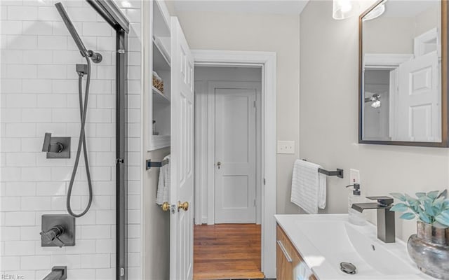 full bath with tiled shower, vanity, and wood finished floors