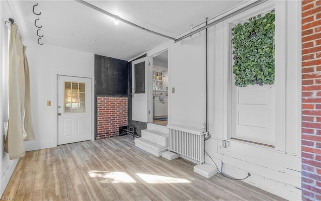 interior space featuring radiator heating unit, wood finished floors, baseboards, and brick wall