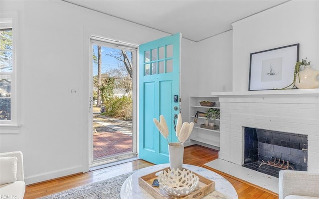 entrance foyer featuring baseboards, plenty of natural light, a brick fireplace, and wood finished floors