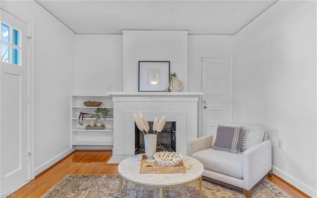 living area featuring baseboards, a brick fireplace, and wood finished floors