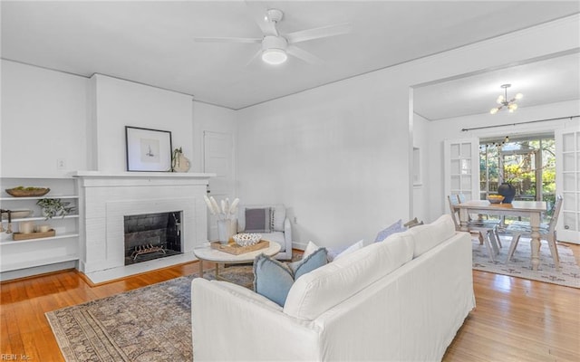 living room featuring ceiling fan with notable chandelier, a fireplace, and wood finished floors