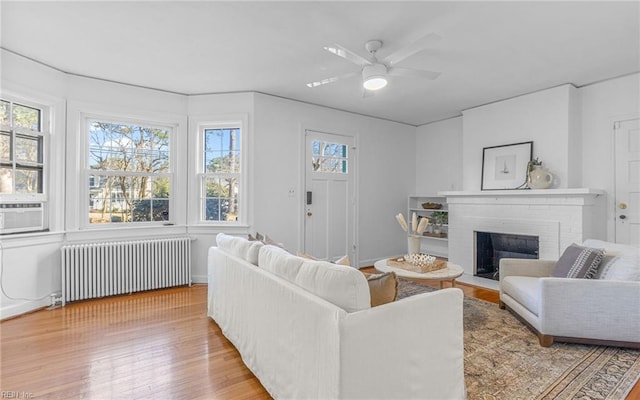 living room featuring a ceiling fan, a brick fireplace, wood finished floors, and radiator heating unit