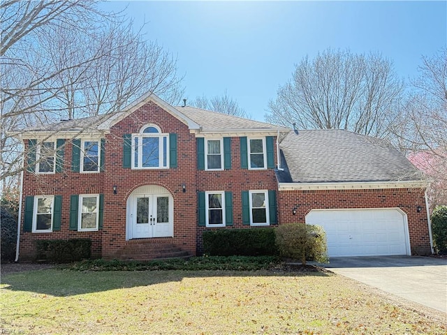 colonial house featuring driveway, a front lawn, roof with shingles, an attached garage, and brick siding