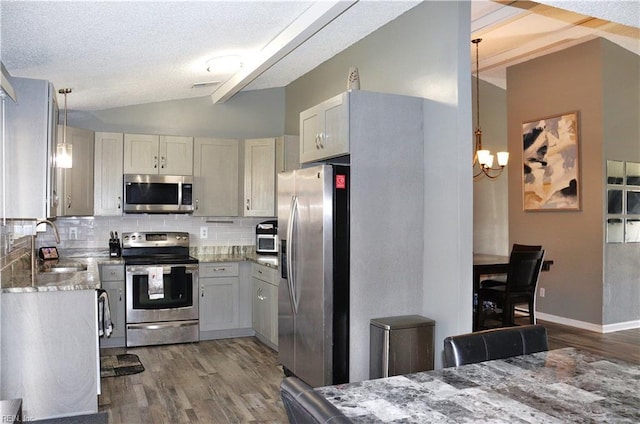 kitchen featuring backsplash, lofted ceiling with beams, appliances with stainless steel finishes, wood finished floors, and a sink