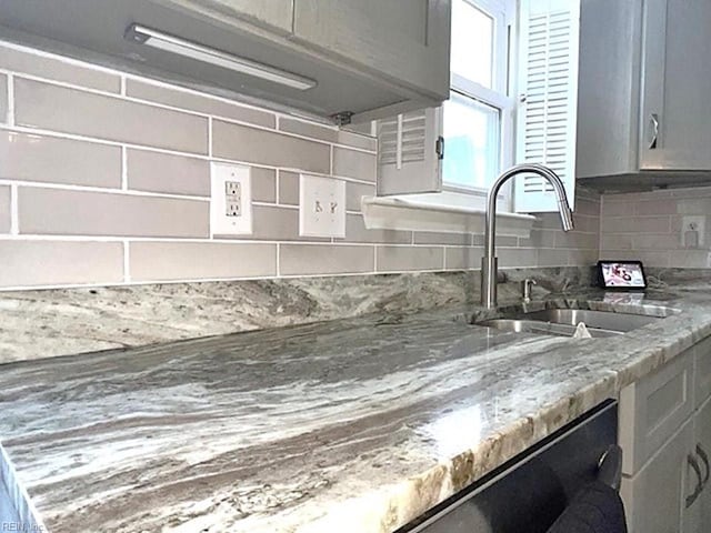 kitchen featuring decorative backsplash, light stone counters, dishwasher, and a sink