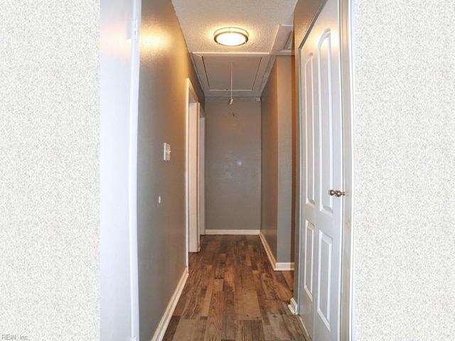 hall with a textured ceiling, attic access, baseboards, and dark wood-style flooring