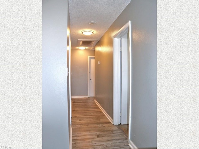 hall featuring baseboards, wood finished floors, visible vents, and a textured ceiling