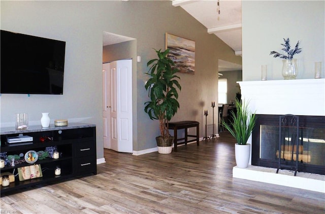 living area featuring baseboards, a multi sided fireplace, wood finished floors, and vaulted ceiling with beams