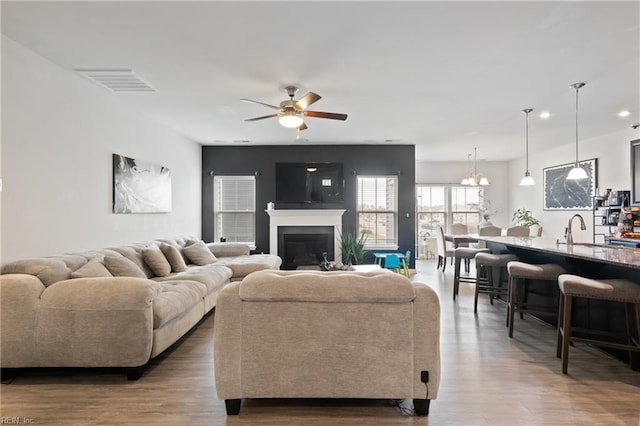 living area featuring a glass covered fireplace, visible vents, wood finished floors, and ceiling fan