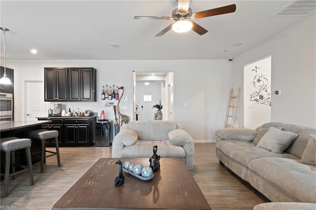 living room featuring visible vents, light wood-style flooring, indoor bar, and a ceiling fan