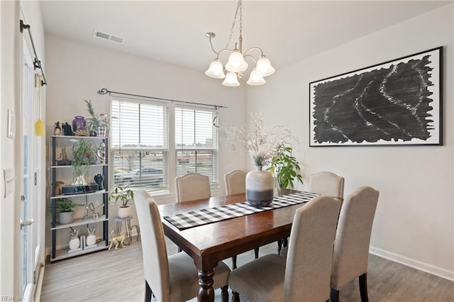 dining area with baseboards, wood finished floors, visible vents, and a chandelier