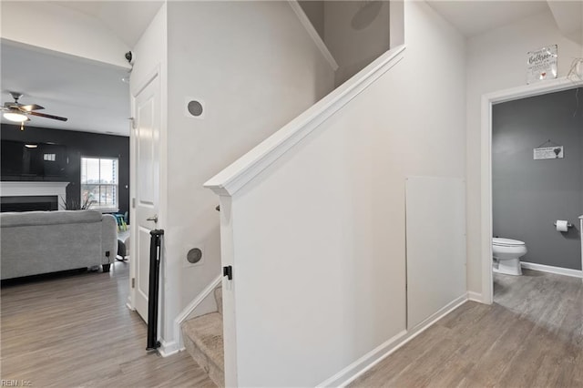 staircase with a fireplace, baseboards, ceiling fan, and wood finished floors