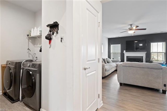 laundry room featuring ceiling fan, washer and clothes dryer, laundry area, light wood-style flooring, and a fireplace