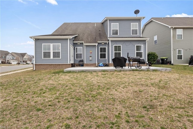 back of property with a lawn, a shingled roof, and a patio area