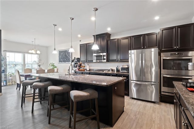 kitchen featuring dark stone countertops, a center island with sink, a sink, stainless steel appliances, and a kitchen breakfast bar