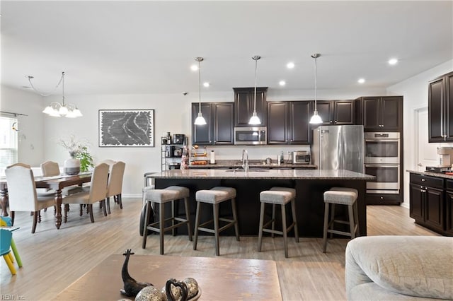 kitchen with a sink, stone counters, appliances with stainless steel finishes, and a breakfast bar