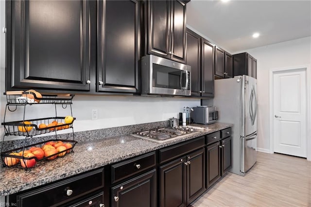 kitchen with dark stone counters, light wood-style flooring, dark cabinets, and appliances with stainless steel finishes