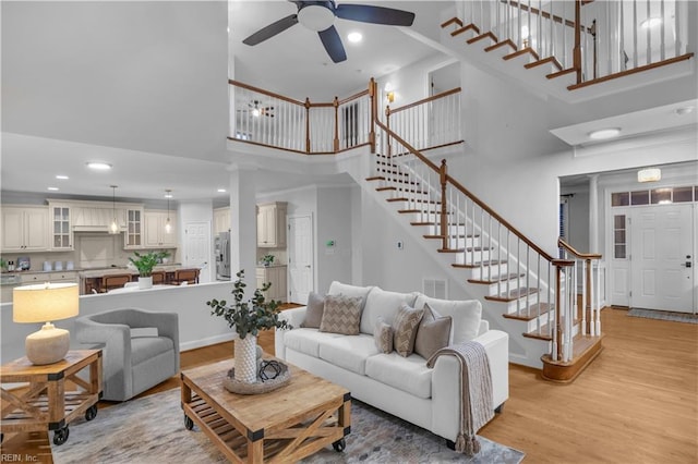 living area with a towering ceiling, visible vents, light wood-style flooring, and stairs