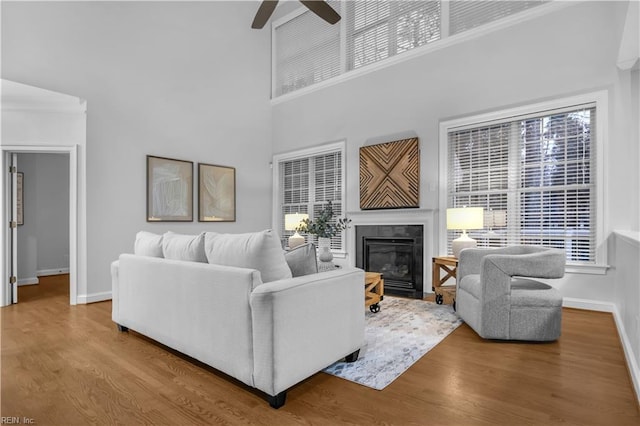 living room with ceiling fan, baseboards, a fireplace with flush hearth, and wood finished floors