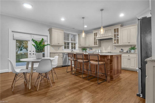 kitchen featuring wood finished floors, premium range hood, appliances with stainless steel finishes, a kitchen breakfast bar, and a center island