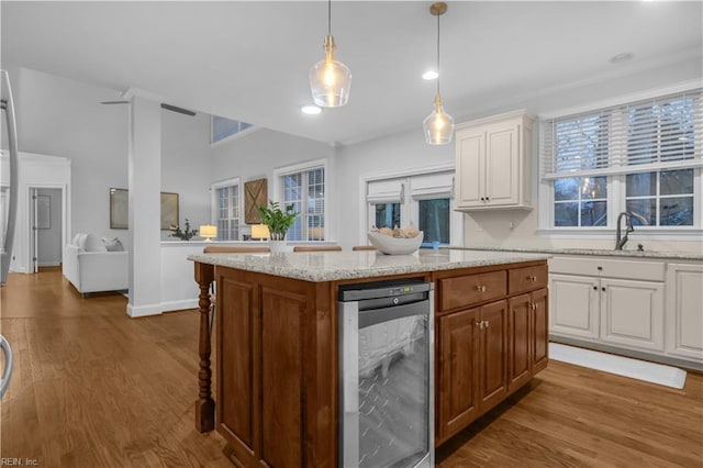 kitchen featuring wood finished floors, a sink, wine cooler, white cabinetry, and a center island