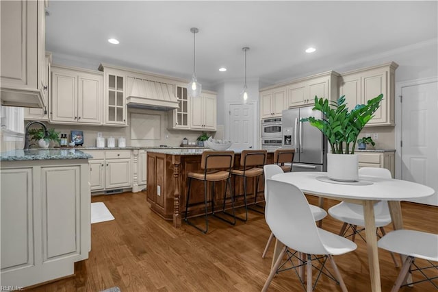 kitchen with custom range hood, dark wood-style floors, a center island, appliances with stainless steel finishes, and a breakfast bar area