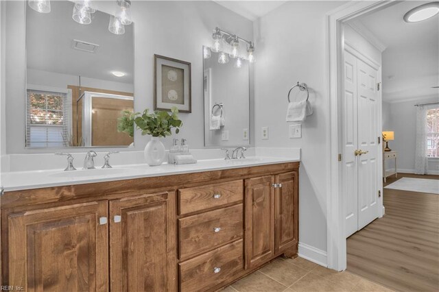 bathroom featuring baseboards, double vanity, a stall shower, tile patterned floors, and a sink