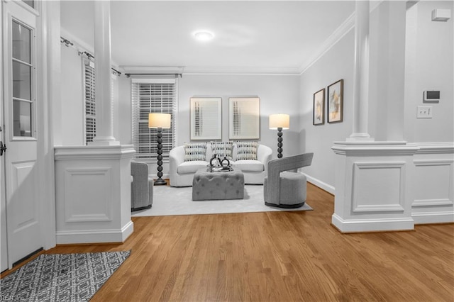 living area with crown molding, light wood-style flooring, decorative columns, and a decorative wall