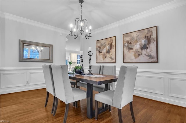 dining room featuring a wainscoted wall, wood finished floors, an inviting chandelier, and ornamental molding