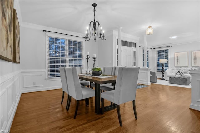 dining space featuring a wainscoted wall, wood finished floors, an inviting chandelier, crown molding, and a decorative wall