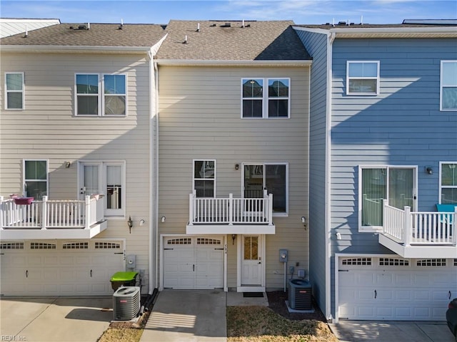 back of property with an attached garage, central AC unit, driveway, and roof with shingles