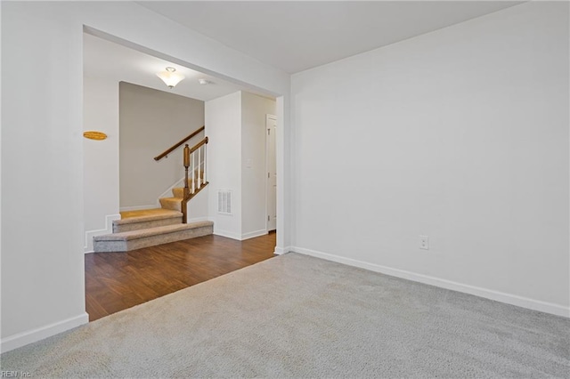 carpeted spare room featuring visible vents, stairs, and baseboards