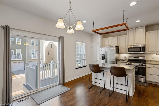 kitchen with light stone counters, dark wood-style floors, visible vents, stainless steel appliances, and a center island