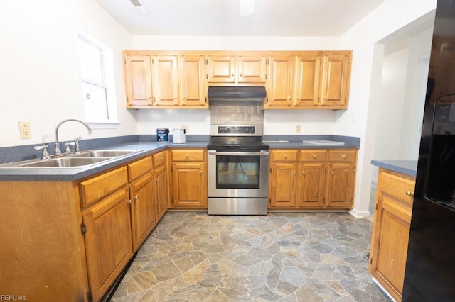 kitchen with electric range, a sink, stone finish floor, under cabinet range hood, and dark countertops