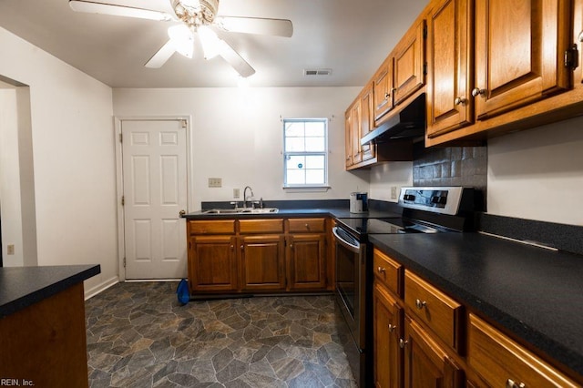 kitchen featuring a sink, stainless steel range with electric cooktop, stone finish floor, under cabinet range hood, and dark countertops