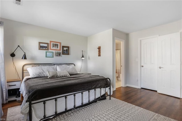 bedroom featuring visible vents, baseboards, ensuite bath, and wood finished floors