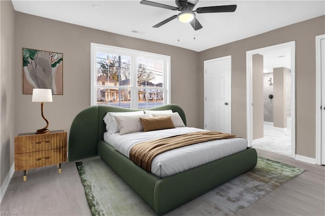 bedroom featuring visible vents, a ceiling fan, ensuite bath, wood finished floors, and baseboards