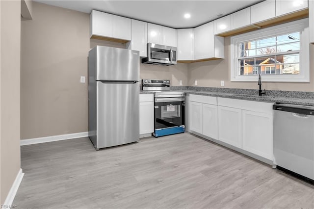 kitchen featuring light wood finished floors, baseboards, appliances with stainless steel finishes, white cabinets, and a sink