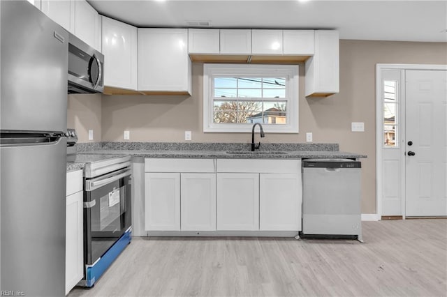 kitchen featuring a sink, light stone counters, appliances with stainless steel finishes, white cabinets, and light wood finished floors